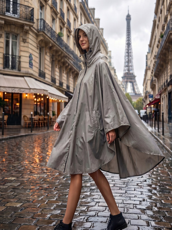 Femme en poncho de pluie gris à capuche, marchant sous la pluie sur des pavés.