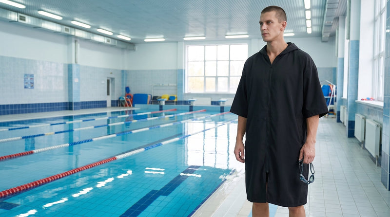 Poncho de surf zippé noir uni porté au bord d'un bassin de piscine intérieure