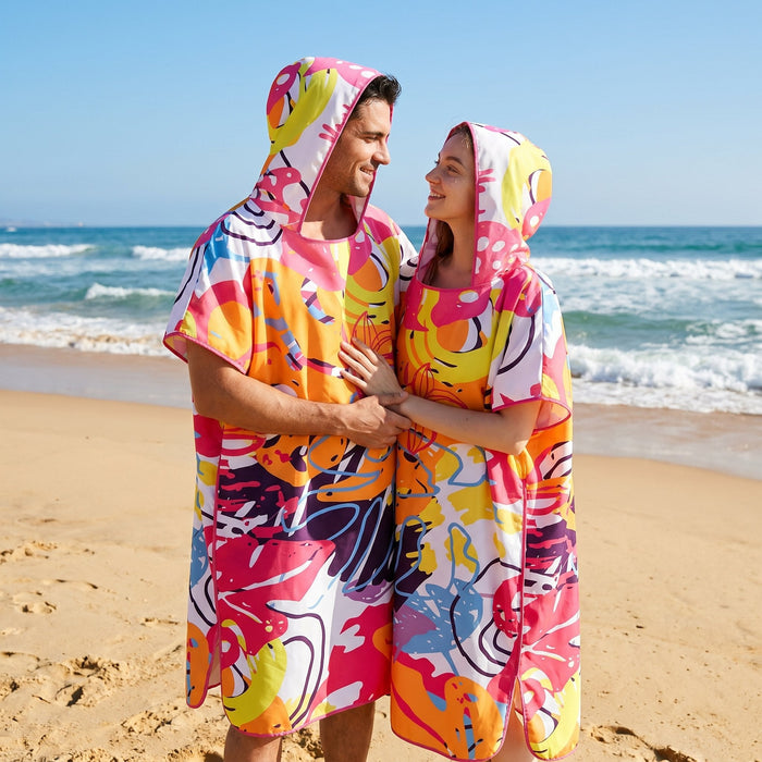 Poncho serviette a capuche motif tropical rose et jaune, porté par un couple souriant sur la plage.