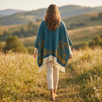 Cape poncho femme ouverte motif turquoise, portée de dos par une femme marchant dans un champ. Les motifs dorés et les