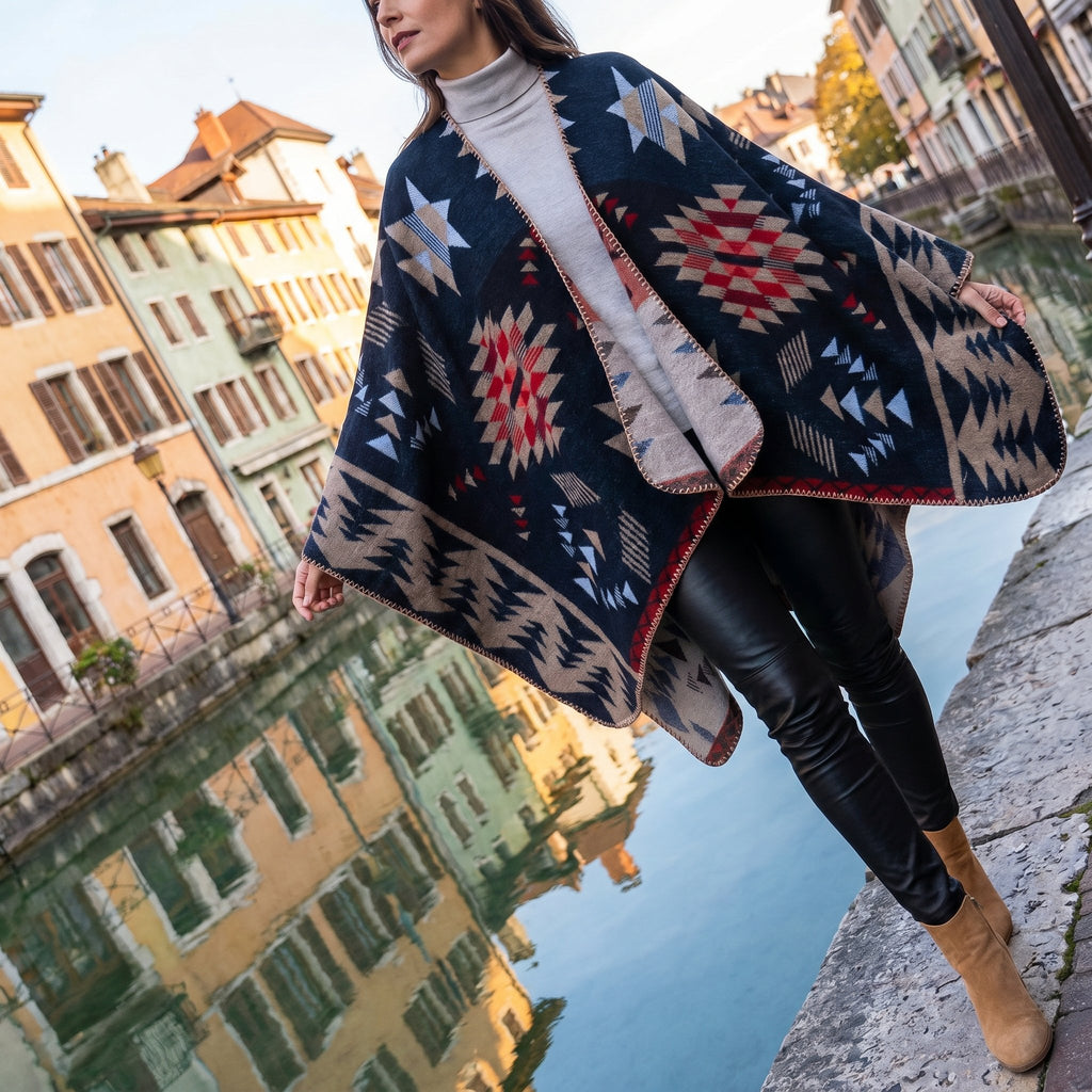 Poncho cape motif Aztèque marine porté par une femme marchant le long d'un canal, vue de profil.