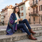 Poncho cape colorblock vert et violet porté par une femme assise sur des marches, tenant une tasse.