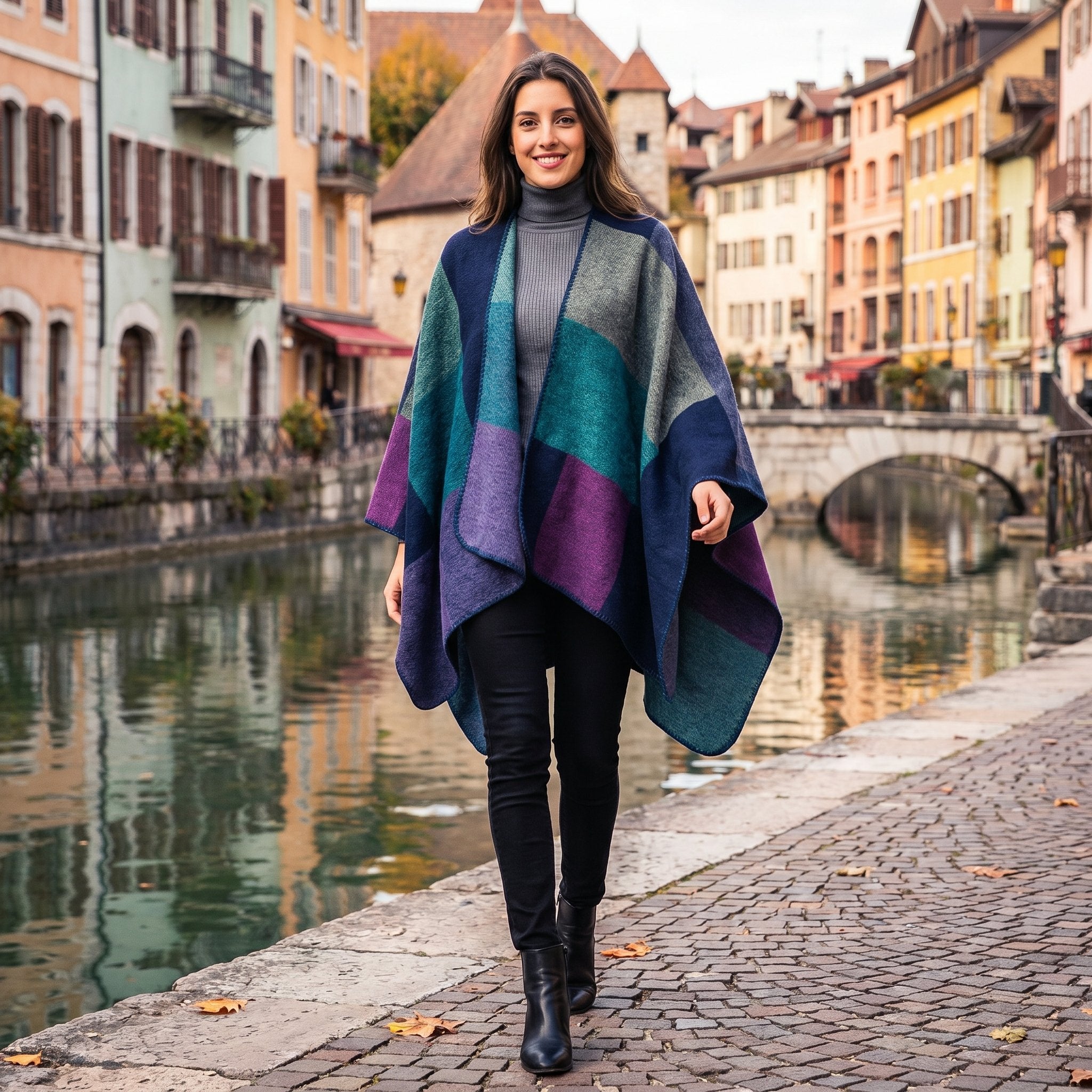 Poncho cape colorblock vert et violet porté par une femme souriante marchant le long d'un canal.