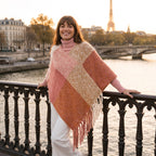 Poncho cape femme colorblock corail porté par une femme souriante posant sur un pont.