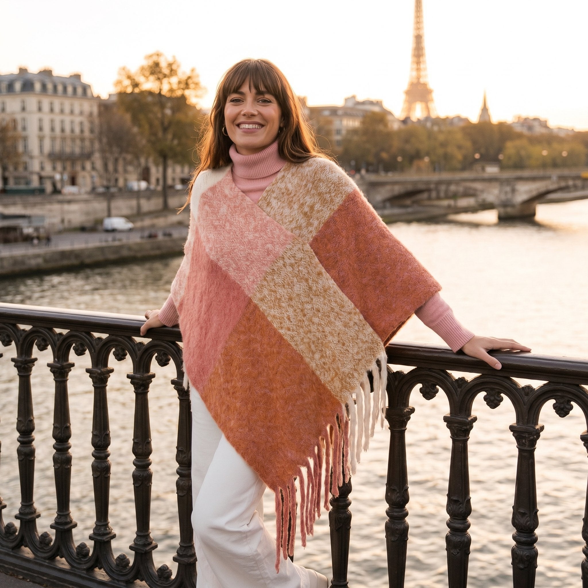 Poncho cape femme colorblock corail porté par une femme souriante posant sur un pont.