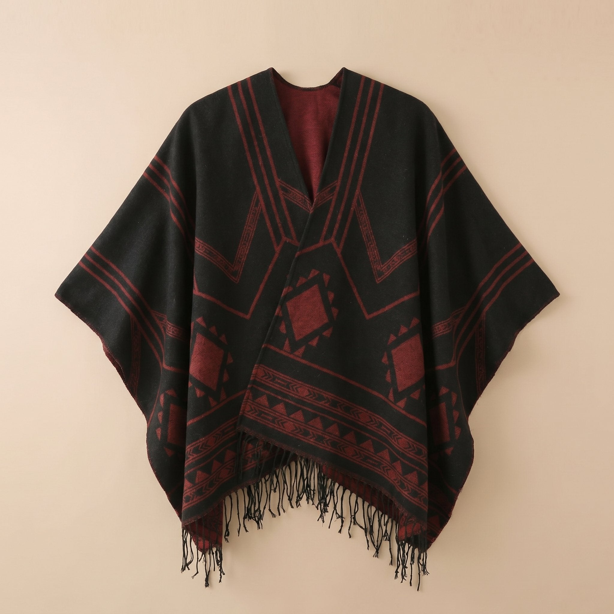Poncho cape femme à motif géométrique et franges noir et rouge, présenté à plat sur un fond clair, vue de face