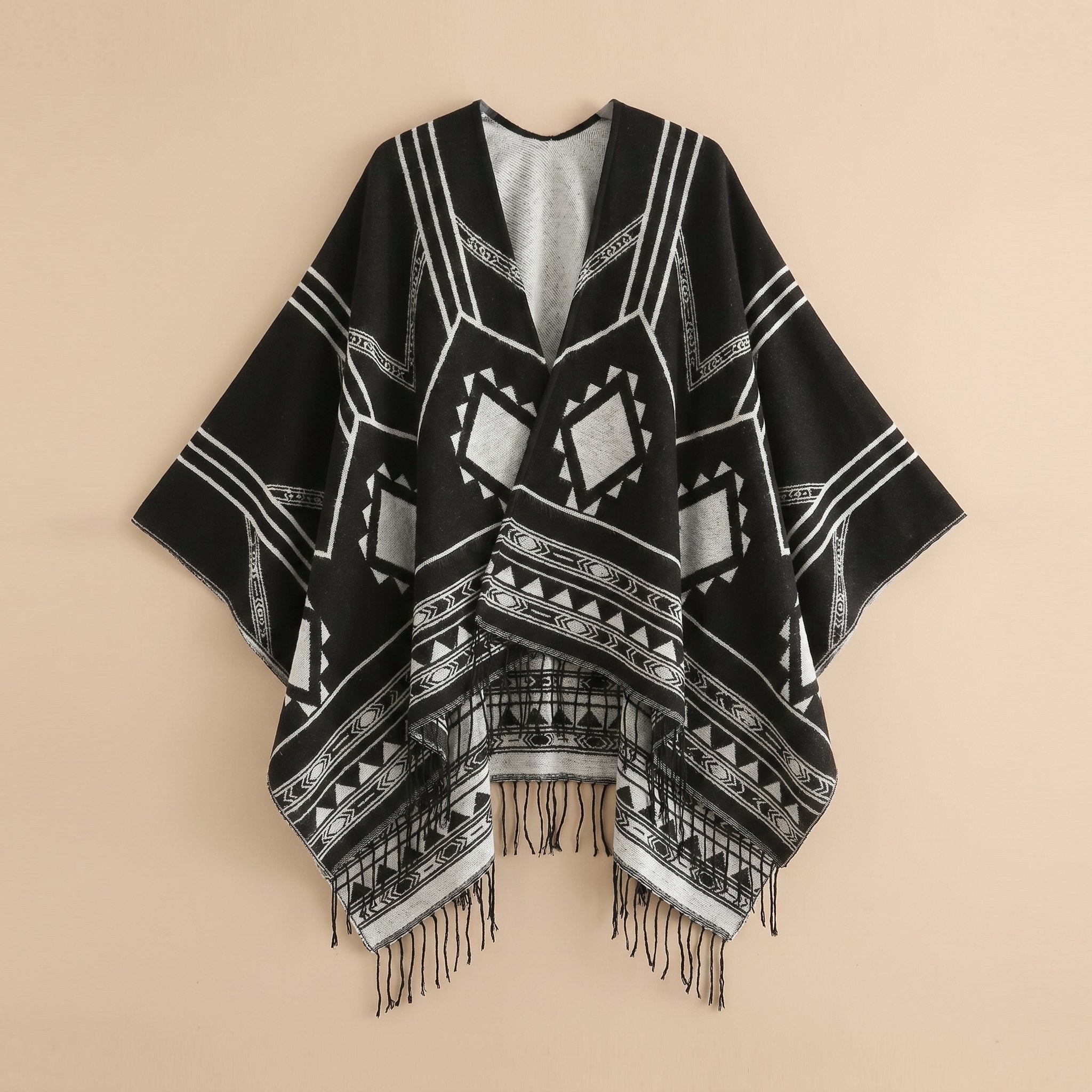 Poncho cape femme à motif géométrique et franges noir et blanc, présenté à plat sur un fond clair, vue de face