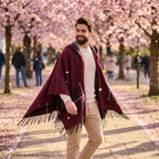 Poncho cape homme à carreaux avec poches bordeaux, porté par un homme marchant sous des arbres fleuris aux pétales roses
