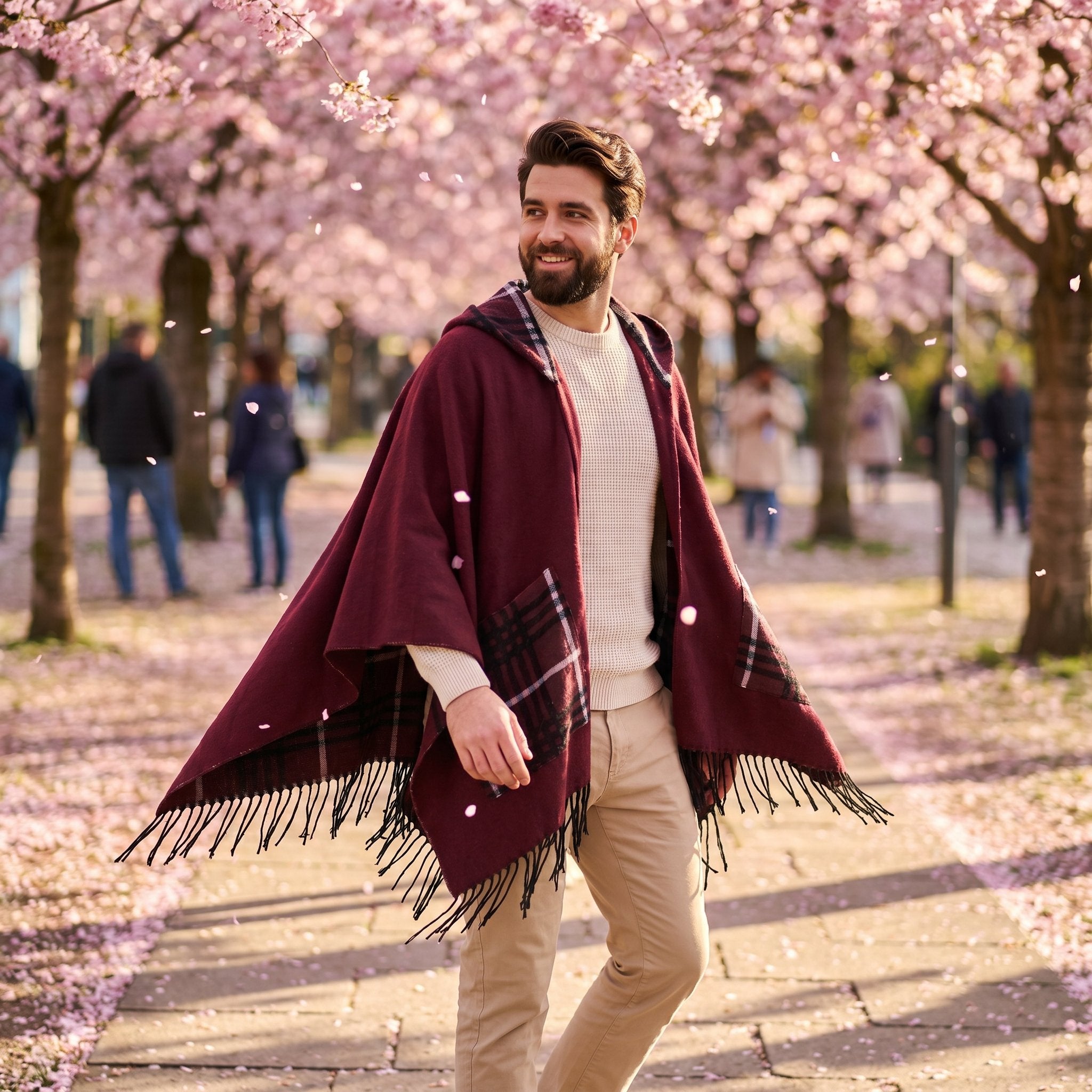 Poncho cape homme à carreaux avec poches bordeaux, porté par un homme marchant sous des arbres fleuris aux pétales roses