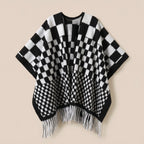 Poncho cape homme à damier noir et blanc, posé à plat de face, montrant les franges blanches
