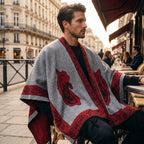 Poncho cape homme à médaillon gris et rouge, porté par un homme assis à une table de café en extérieur