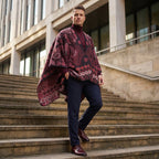 Poncho cape homme paisley bordeaux, porté par un homme de face, descendant des escaliers extérieurs, avec un pull col roulé