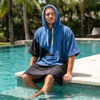 Poncho serviette à capuche bicolore bleu et noir, porté par un homme au bord d'une piscine.