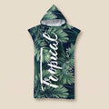 Poncho serviette à capuche motif feuillage tropical, présenté à plat sur un fond beige uni.