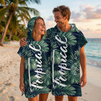 Poncho serviette à capuche motif feuillage tropical, porté par un couple souriant sur une plage.