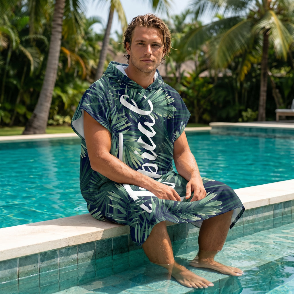Poncho serviette à capuche motif feuillage tropical, porté par un homme assis au bord d'une piscine.