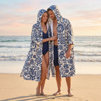 Poncho serviette à capuche motif fleurs bleues, porté par un couple debout sur une plage de sable.