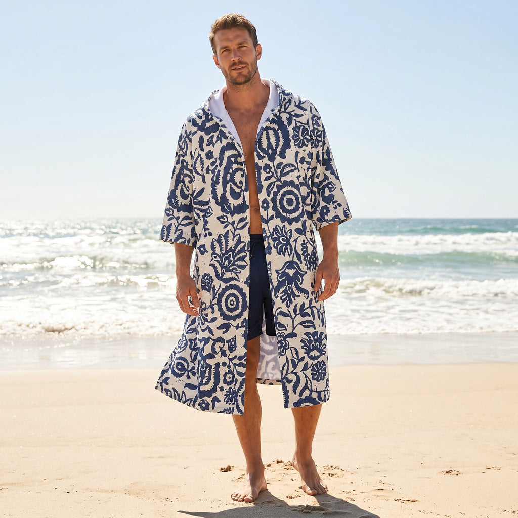 Poncho serviette à capuche motif fleurs bleues, porté par un homme debout sur la plage.