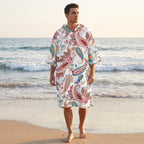 Poncho serviette a capuche motif paisley colore, porte par un homme debout sur la plage.