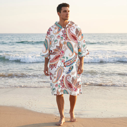 Poncho serviette a capuche motif paisley colore, porte par un homme debout sur la plage.