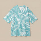 Poncho serviette à capuche motif palmes turquoise, posé à plat sur un fond uni beige.
