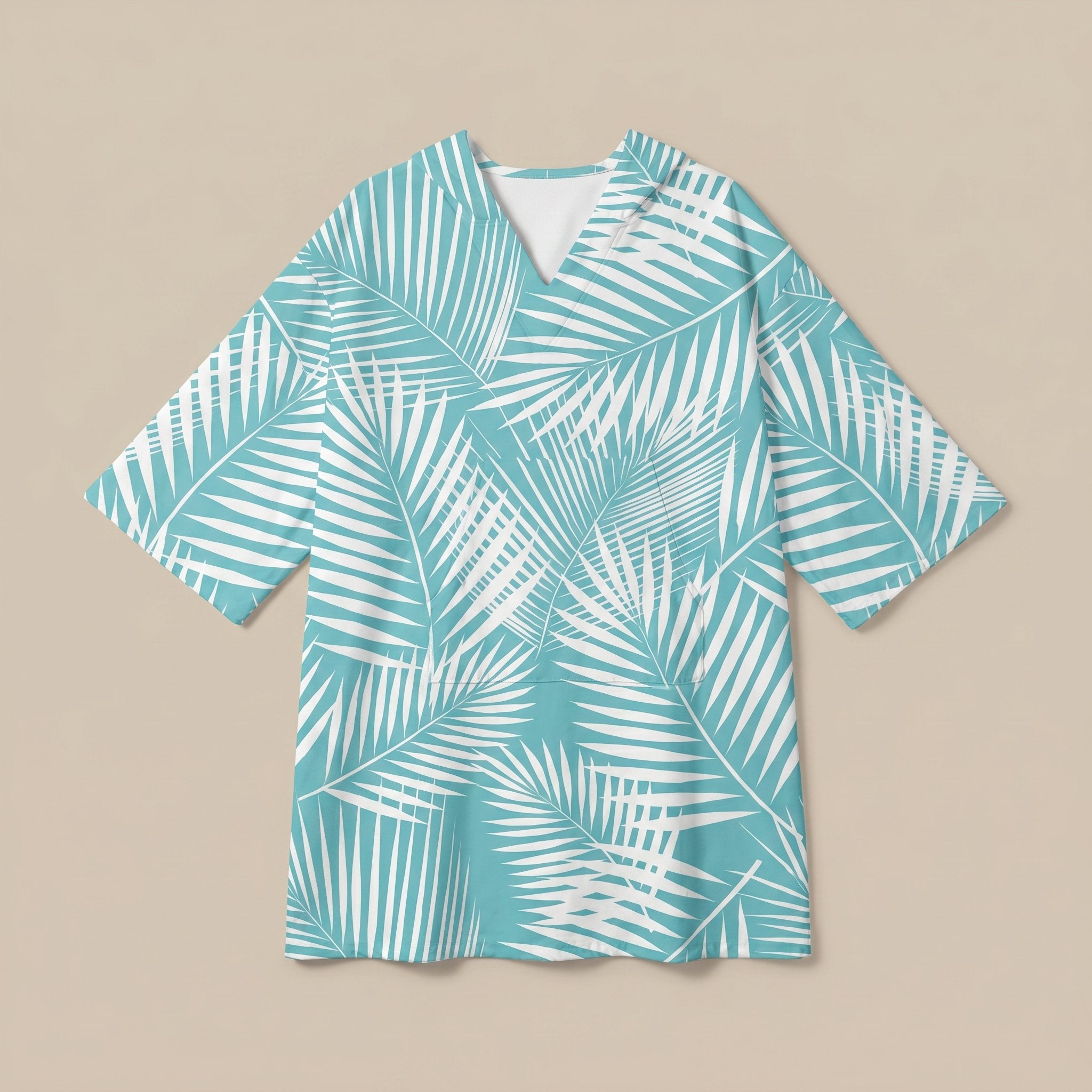 Poncho serviette à capuche motif palmes turquoise, posé à plat sur un fond uni beige.
