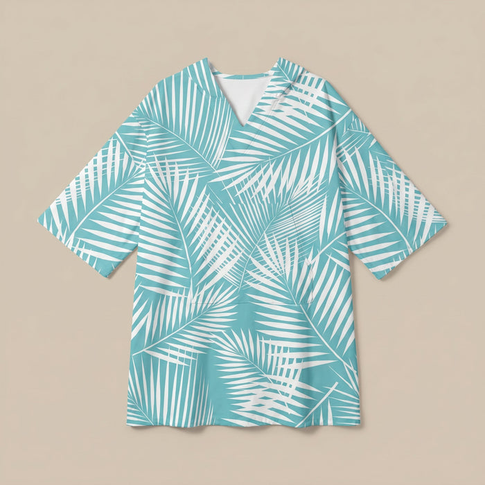 Poncho serviette à capuche motif palmes turquoise, posé à plat sur un fond uni beige.