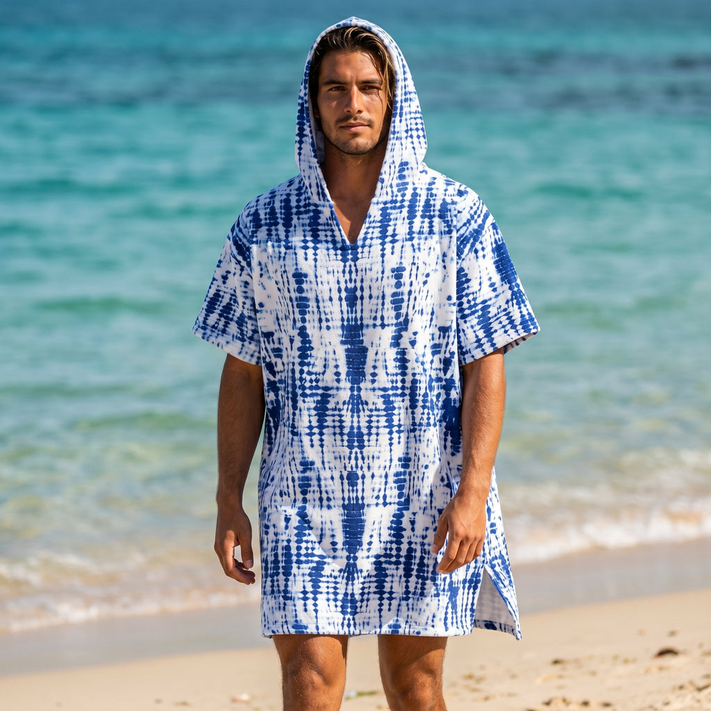 Poncho serviette a capuche motif tie-dye bleu, porté par un homme debout sur une plage face à la mer.