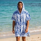 Poncho serviette a capuche motif tie-dye bleu, porté par un homme debout sur une plage face à la mer.