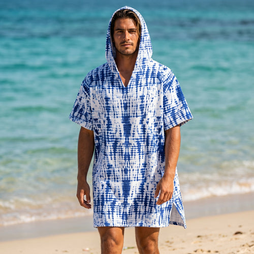 Poncho serviette a capuche motif tie-dye bleu, porté par un homme debout sur une plage face à la mer.