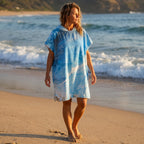 Poncho serviette a capuche motif Vague bleue, porte par une femme marchant sur la plage.