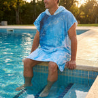 Poncho serviette a capuche motif Vague bleue, porte par un homme assis au bord d'une piscine.