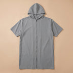 Poncho de bain zippé gris uni posé à plat sur un fond beige clair, montrant la fermeture éclair centrale.