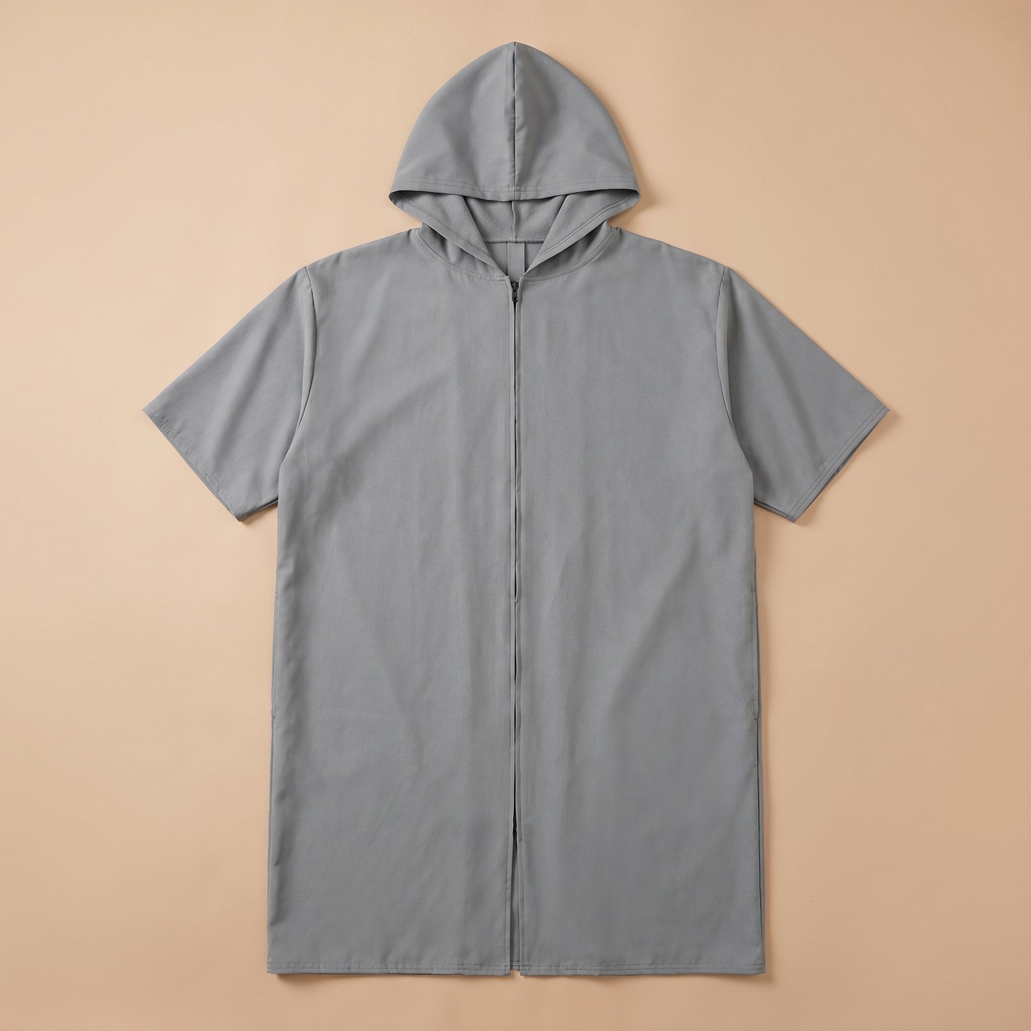 Poncho de bain zippé gris uni posé à plat sur un fond beige clair, montrant la fermeture éclair centrale.