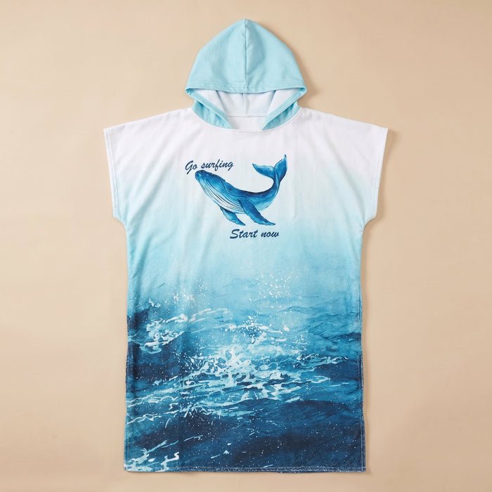 Poncho serviette à capuche motif baleine bleue, posé à plat sur un fond beige uni.