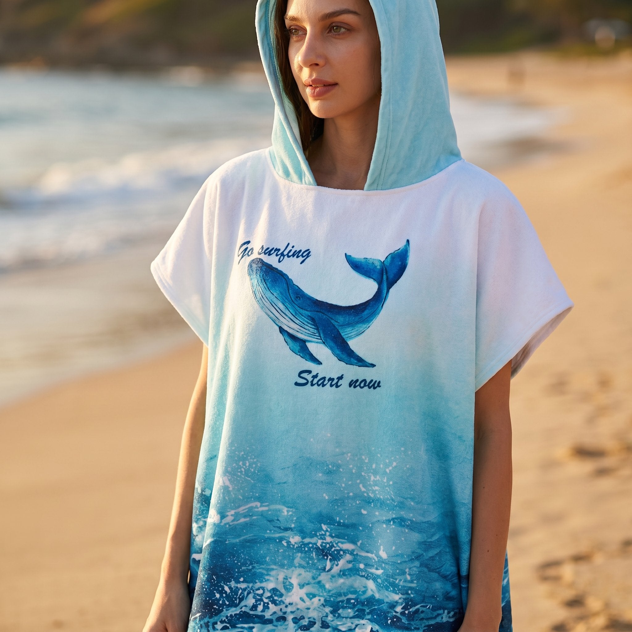 Poncho serviette à capuche motif baleine bleue, gros plan sur le haut du vêtement porté par une femme sur la plage.