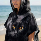 Poncho serviette à capuche motif chat noir, porté par une femme, cadrage serré sur le buste et le visage.
