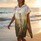 Poncho serviette à capuche motif chevaux au couchant, porté par une femme marchant sur le sable.