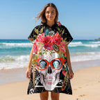 Poncho serviette à capuche motif crâne à lunettes, porté par une femme souriante sur la plage.