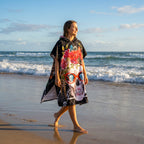Poncho serviette à capuche motif crâne à lunettes, porté par une femme marchant au bord de l'eau.