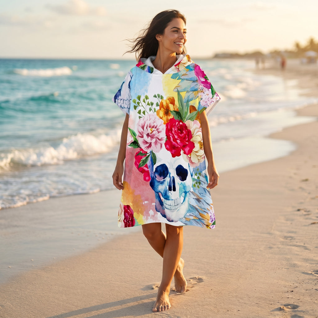 Poncho serviette à capuche motif crâne fleuri, porté par une femme marchant sur la plage.