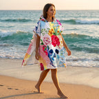 Poncho serviette à capuche motif crâne fleuri, porté par une femme marchant de profil sur le sable.