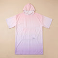Poncho serviette à capuche motif dégradé rose, présenté à plat sur un fond beige uni.