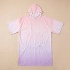 Poncho serviette à capuche motif dégradé rose, présenté à plat sur un fond beige uni.