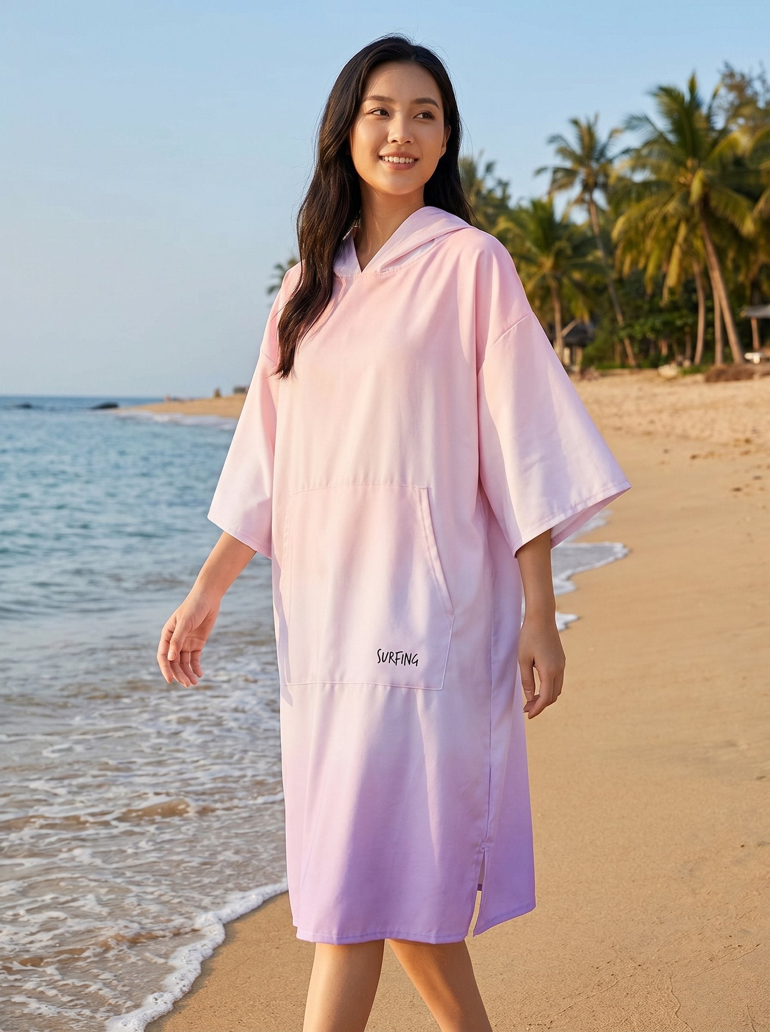 Poncho serviette à capuche motif dégradé rose, porté par une femme marchant sur la plage.