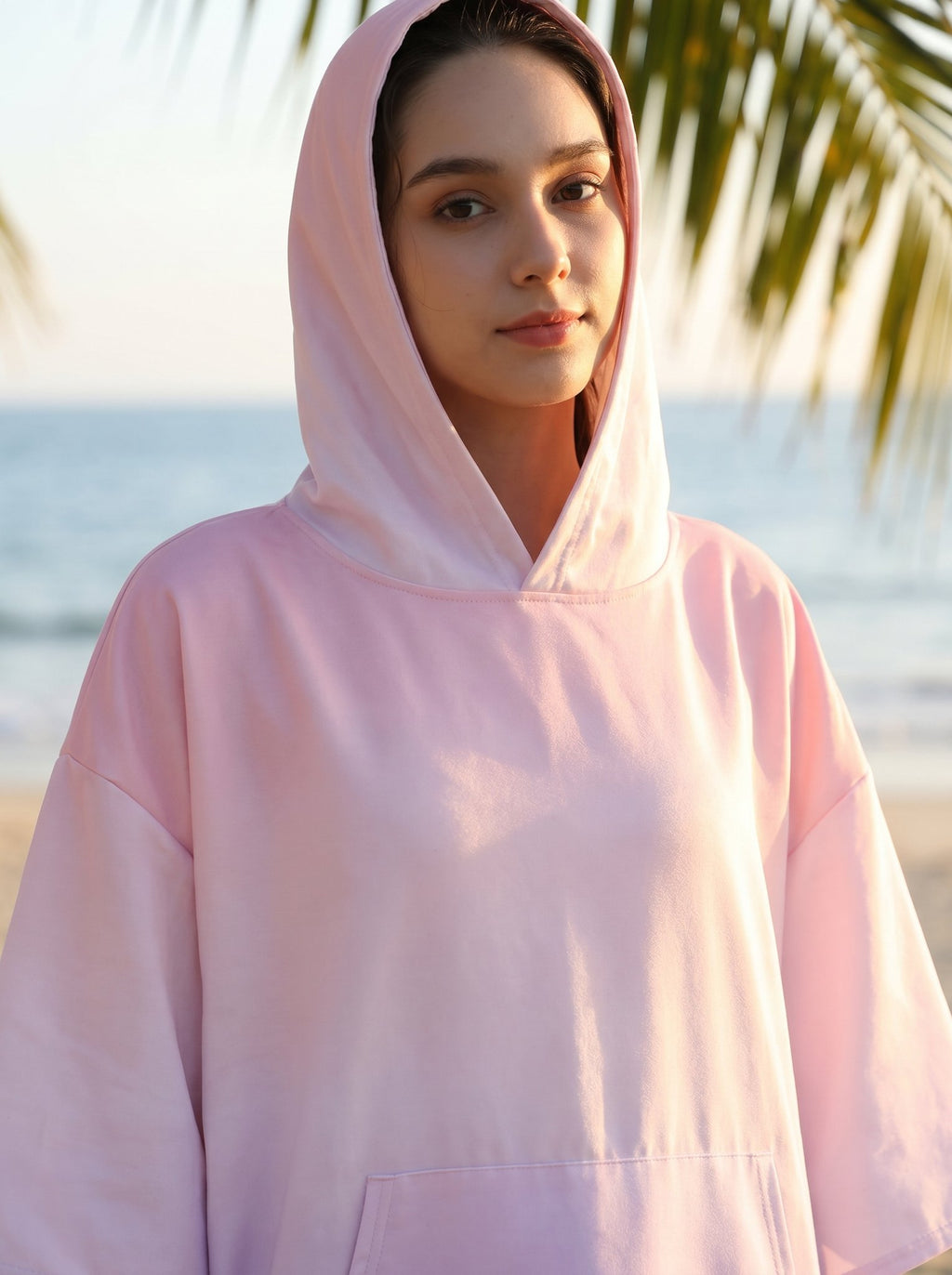 Poncho serviette à capuche motif dégradé rose, porté par une femme en gros plan sur la plage.