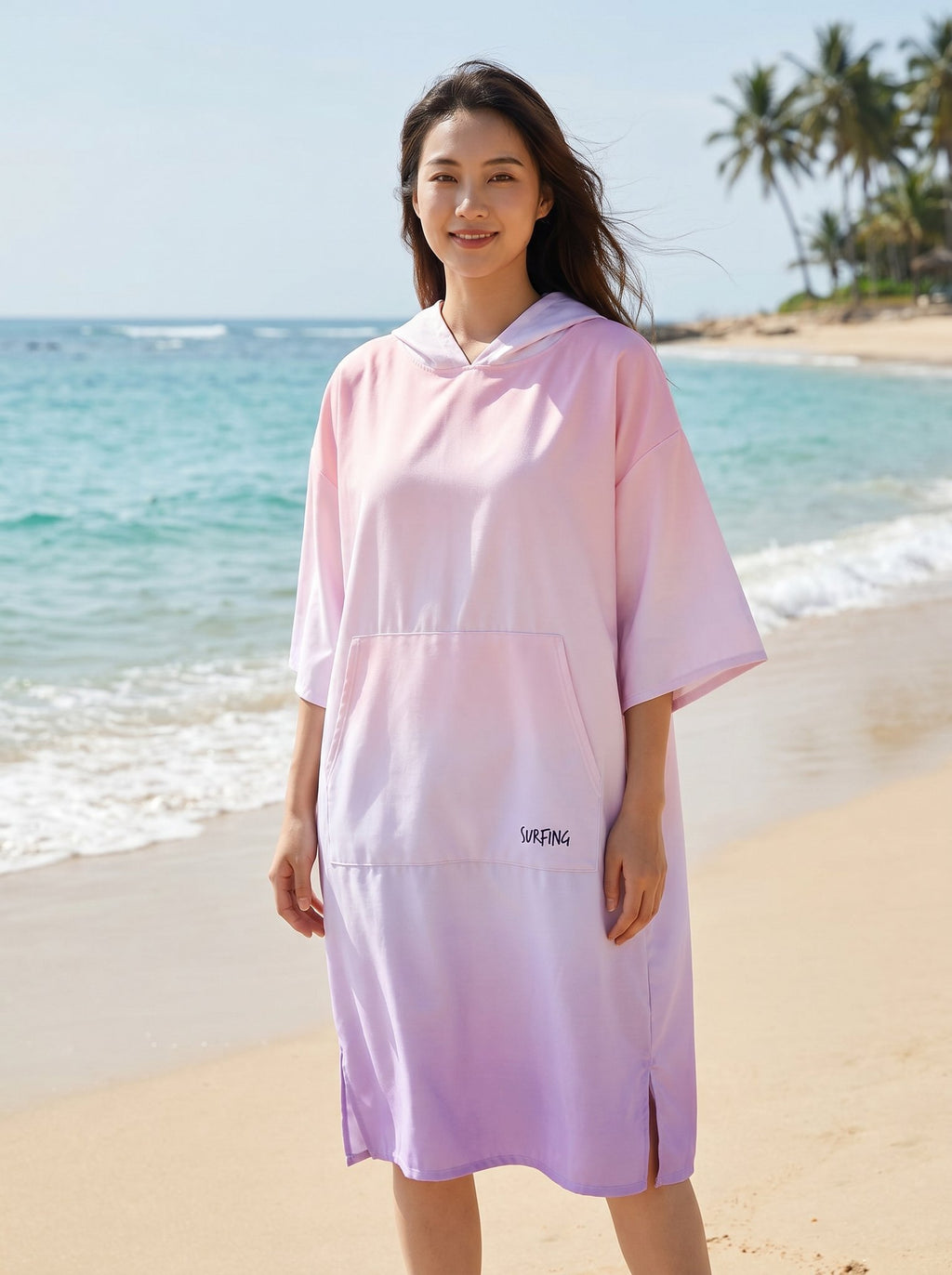 Poncho serviette à capuche motif dégradé rose, porté par une femme debout de face sur la plage.