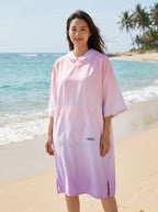 Poncho serviette à capuche motif dégradé rose, porté par une femme debout de face sur la plage.