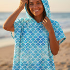 Poncho serviette à capuche motif écailles bleu ciel, porté par une femme souriante en gros plan.