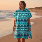 Poncho serviette à capuche motif aztèque bleu porté par une femme de profil sur une plage au coucher du soleil.